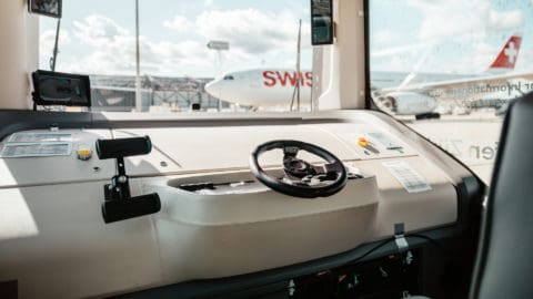 Unoccupied driver position of a Zurich Airport automated shuttle, with SWISS aircraft on the apron in the background