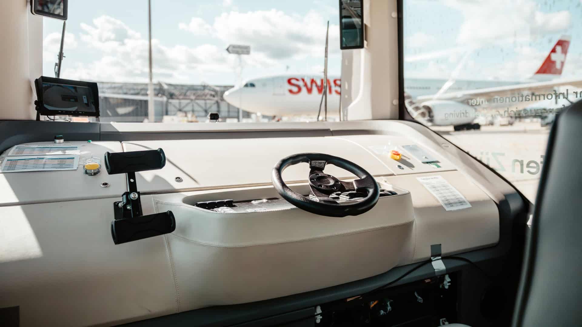 Unoccupied driver position of a Zurich Airport automated shuttle, with SWISS aircraft on the apron in the background